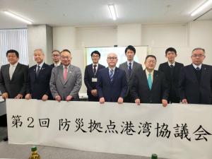 6名の関係者の方々が「第2回 防災拠点港湾協議会」と書かれた幕を持ち、その後ろに4名の関係者の方が並んで記念撮影をしている写真
