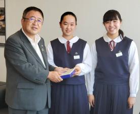 横並びに立つ制服を着た女子中学生2名のうち1名が義援金を市長に渡し、市長が受け取っている様子の写真