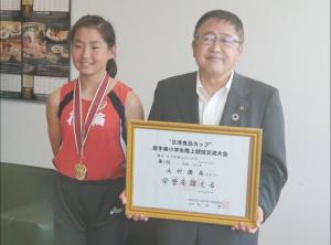 ユニフォームを着て首からメダルを下げている女の子と、隣で賞状の額縁を持っている市長が並んで写っている写真