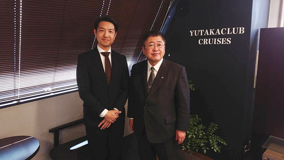 黒色で統一された室内で、クルーズのゆたか倶楽部の松浦賢太郎代表取締役と市長が並んでいる写真