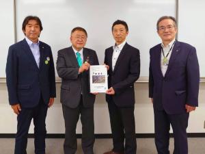 要望書正面に向け一緒に持つ市長とスーツを着た男性、その2人の両端に立つ関係者の男性2名の記念写真