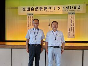 壇上に「全国自然敬愛サミット2022」と書かれた横断幕が掲げられ、その下で起立して並ぶ男性と市長の写真