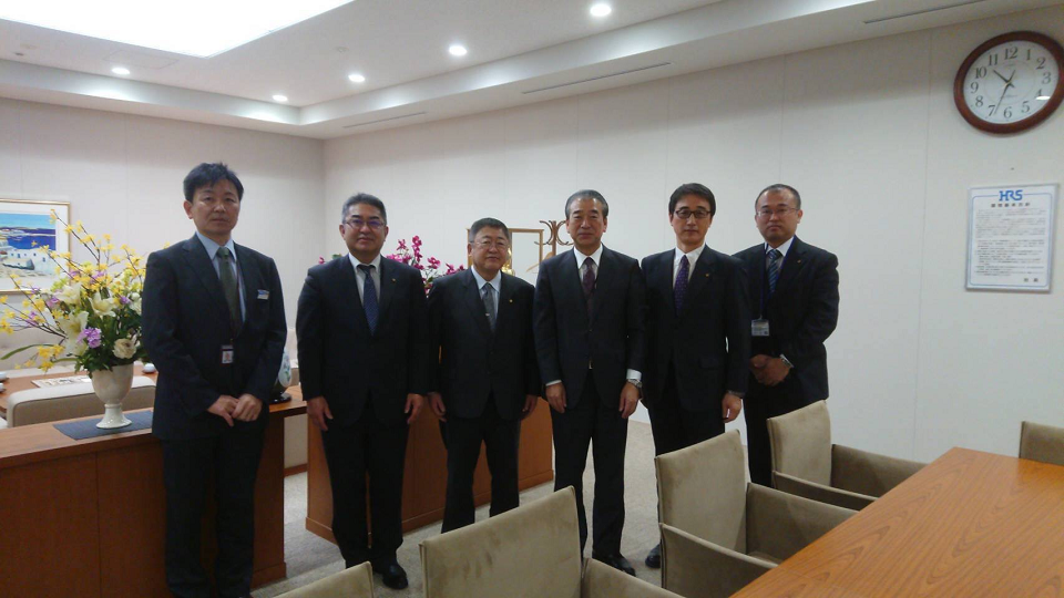 ヒロセ電機株式会社の応接室内で、石井和徳代表取締役社長と石田光生MPC事業部長、市長と副市長と2名の関係者が横一列に並んでいる写真