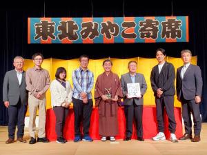 東北みやこ寄席と書かれた横断幕や金屏風をバックに、市長や着物を着た落語家の方など関係者8名が並んだ写真