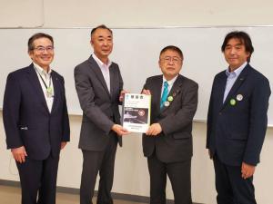 要望書正面に向け一緒に持つ市長とスーツを着た男性、その2人の両端に立つ関係者の男性2名の記念写真