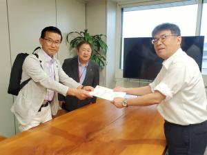 市長の横に立っている山田司郎名取市長が机越しに男性に要望書を渡してる写真