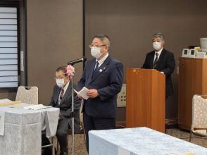 スーツ姿の市長がピンク色のリボンが飾られたマイクスタンドの前に立ち日中友好協会定期総会で参加された方々に対してあいさつを述べている写真
