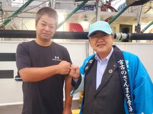 港の関係者の男性と青色の法被を着た男性が右手の握りこぶしを突き合わせてポーズをとっているところを写した写真
