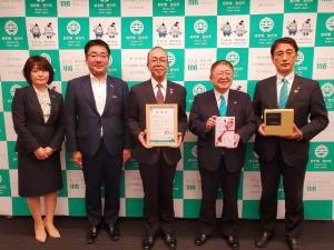 左端に女性が立ち、その右側に市長含む4名の男性が並び、中央の男性が感謝状、右から二番目の市長が目録、右端の副市長がサウンドアーチを持っている記念写真