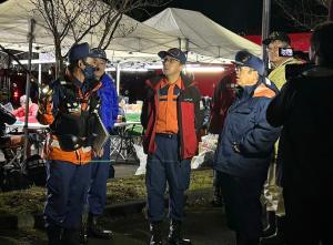 テントが設置された傍で、市長や4名の関係者が輪になり話をしている様子を右側に男性が立ち撮影している様子の写真