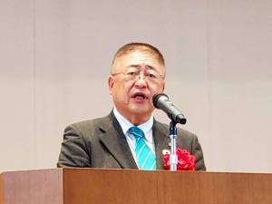左胸に胸章リボンを付けた市長が檀上で挨拶を行っている様子をアップで撮影した写真