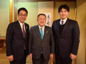 掛け軸が飾られた室内で、市長を含め男性3名が並んでいる写真