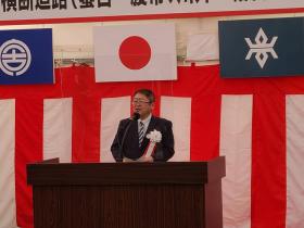 開通式の会場で紅白の幕を背景に市長が演台で、あいさつを述べている写真