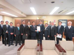 ベージュ色の応接椅子が設置された室内で、農林水産省農産局長の平形雄策氏と市長会の代表が一緒に要望書を持って中央に立ち、市長を含む11名の関係者が横一列に並んでいる写真