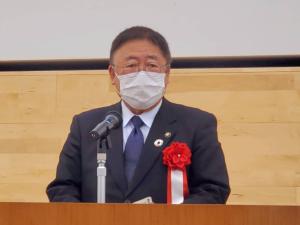 赤い胸章を着けた市長が、マイクの前で話をしている写真