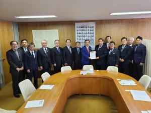 会議室の壁側に自由民主党総務会長の遠藤利明氏と市長会の代表が一緒に要望書を持って中央に立ち、市長を含む12名の関係者が横一列に並んでいる写真