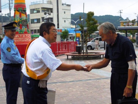 警察官の横に立っている市長が男性に交通安全の街頭広報と黄色い羽根街頭配布をしている様子の写真