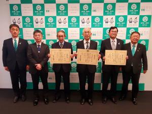 左からスーツを着た男性が2人、賞状を正面に掲げて立つ男性が3人、一番右端に市長が立ち横に並んでいる記念写真