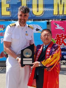白い制服を着た客船の船長と法被を着た市長が2人で記念盾を持っている写真