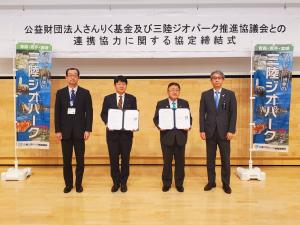 「三陸ジオパーク」と書かれた幟が会場の両端に置かれ、その中央に締結書を両手で持った市長と男性、両端に男性が2名横並びになっている写真