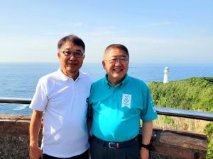 背景に水平線が広がる展望台のような場所で撮影された、市長と男性がカメラに笑顔を向けている写真