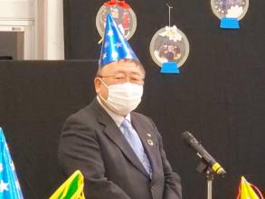 銀色の星マーク模様の青色の三角帽子を被った市長がマイクスタンドの前で挨拶を行っている様子をアップで撮影した写真