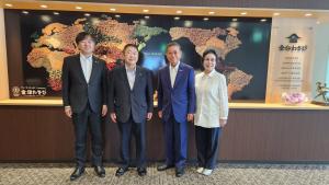 世界地図が飾られた壁の前に、市長、小林会長、小林桂子副会長、石川良市取締役社長が並んでいる写真