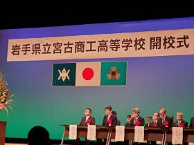 岩手県立宮古商工高等学校開校式と書かれた横断幕のステージ上に市長の他、来賓の方々が赤の胸章をつけて座っている写真