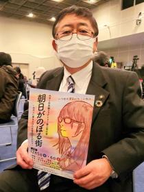 市長が、会場で朝日がのぼる街のパンフレットが見えるように持っている写真