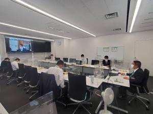 画面が映し出されたモニターが前方に設置された部屋に、机と椅子がコの字型に並べられ、その机に座る市長と関係者6名を写した写真