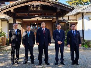 白壁の本館に「臨江閣」と書かれた扁額が弓なりにカーブした大きな庇に配置された玄関前に、市長と4名の関係者が横一列に並んでいる記念写真