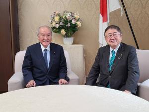 花が生けられた花瓶や国旗が飾られた大臣室で、財務省の鈴木俊一財務大臣と市長が一人掛けのソファに座っている写真