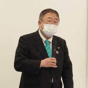 右手に持ったマイクを白いマスクを着けた口元に向け立って話をしている市長の写真