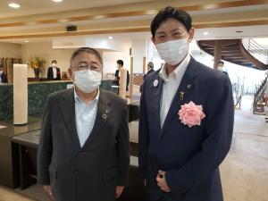 港湾都市協議会総会の会場のロビーで、ピンク色の胸章リボンを付けた関係者の男性と市長が並んでいる写真