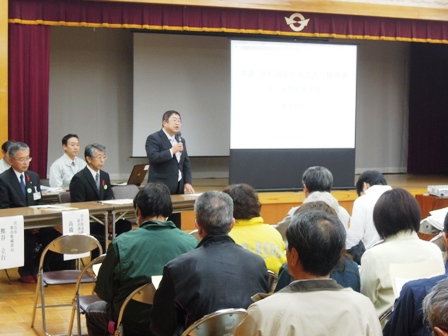 舞台にスクリーンが設置され、その横で市長と関係者が向かい合わせに座っており、参加者に向けて立って話をする市長の写真