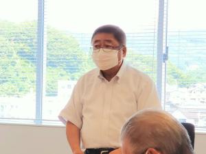 ブラインドカーテンが掛けられた窓を背にし、立って話をする様子の市長の写真