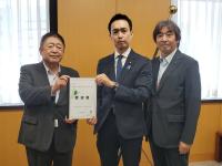 部屋の窓側の位置で市長を含む男性3名が並んで立ち、市長と男性で要望書を持っている写真