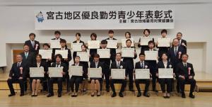 宮古地区優良勤労青少年表彰式の横断幕の前に30名弱の関係者が3列に並び、受賞者の方々が賞状を持っている集合写真