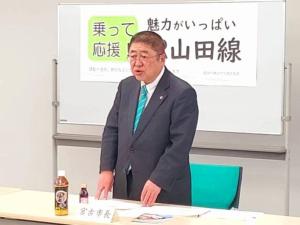 宮古市長と書かれた名札が置かれた長机で両手を机に置き立ちながら話をしている市長の写真