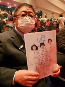 岬のマヨイガのパンフレットの表紙が見えるように市長が観客席に座っている写真