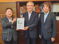 シーサーが飾られた棚の前で、市長を含む男性3名が並んで立ち、市長と男性で要望書を持っている写真