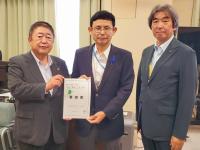 カーテンが少し開いている部屋で市長を含む男性3名が並んで立ち、市長と男性で要望書を持っている写真