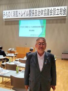 「みちのく潮風トレイル関係自治体協議会設立総会」と書かれた横断幕や資料の表紙が映し出さされた会場に立つ市長の写真