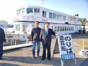 停泊している遊覧船をバックに遊覧船のりばの看板の横に立つ市長と男性の写真