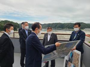 建物の屋上でパネルを見せている様子の男性と、その周りでパネルを見つめる市長と関係者たちの写真