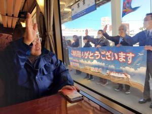 電車の中からホームに向かって手を振る市長と、ホームで横断幕を掲げている方達を写した写真