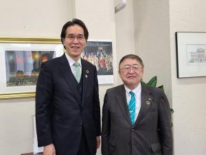花火が描かれた絵画やカレンダーが飾られた壁の前で、青山学院の山本与志春院長と市長が並んでいる写真