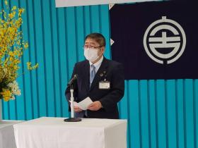 市長が青色の幕と市章を背景に立ち、閉所式においてあいさつを述べている写真