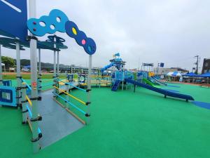 緑の人工芝が敷かれ滑り台などの多くの遊具が置かれた公園の写真