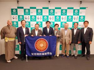 バックパネルの前で「宮古地区保護司会」と書かれた紫色の旗を持った6名の保護司の方々と市長と副市長が横一列に並んでいる写真